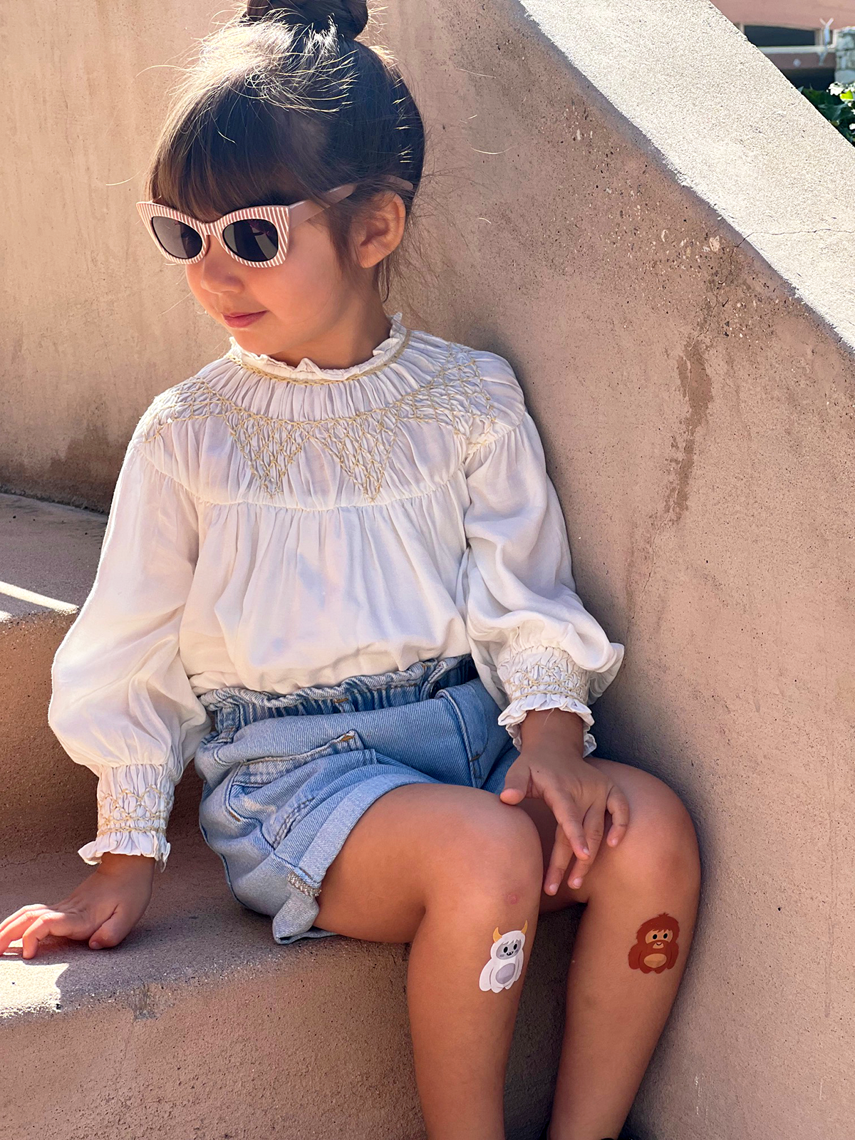 Child sitting outdoors wearing Boo Boo Buddies fun and colorful kids bandages on her knees.
