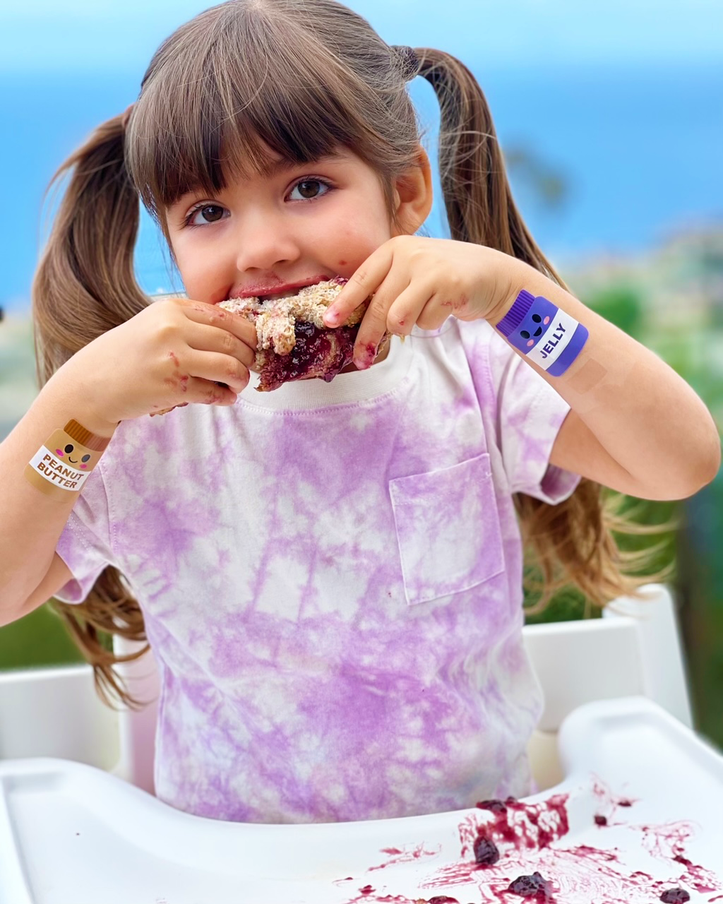 Young child enjoying a snack while wearing Boo Boo Buddies fun and colorful kids bandages on both arms.
